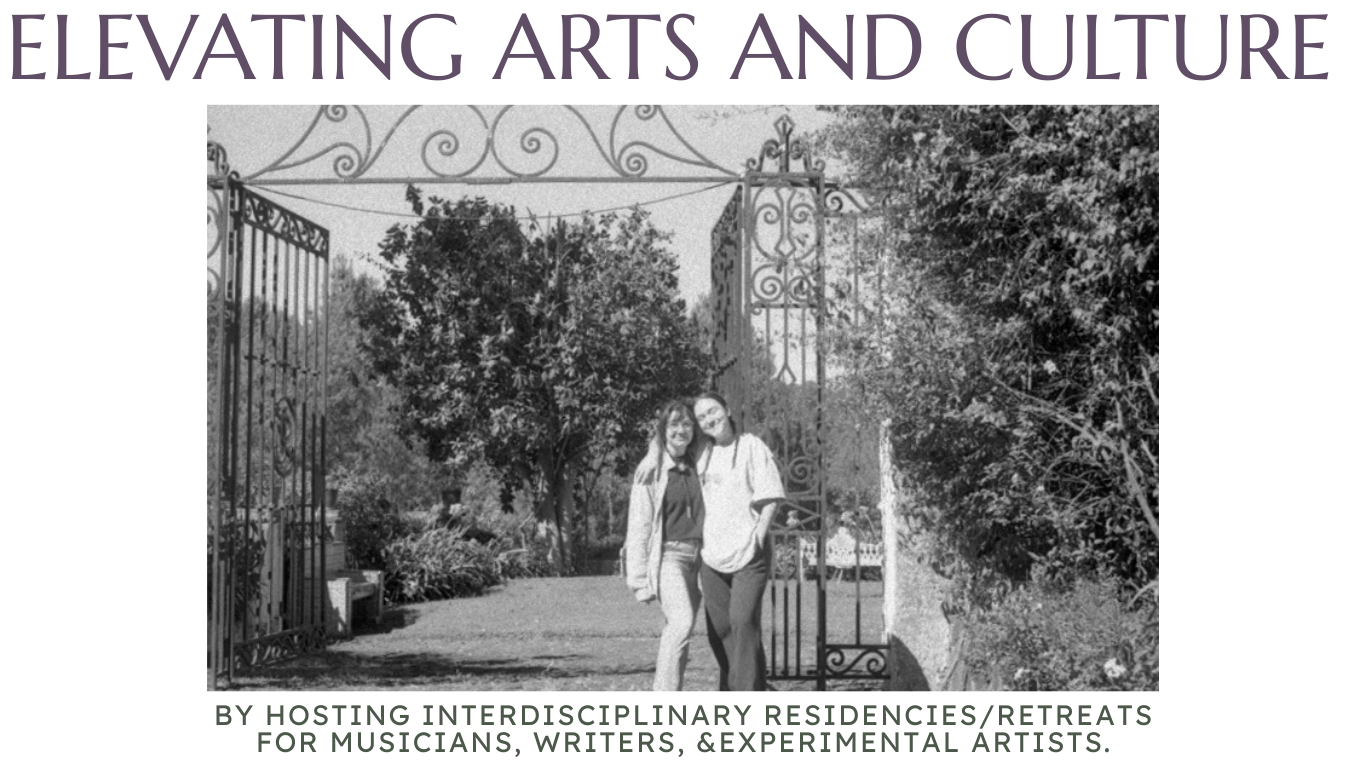 black and white image of two femme artists by an iron fence with swirling flourishes with large trees behind them